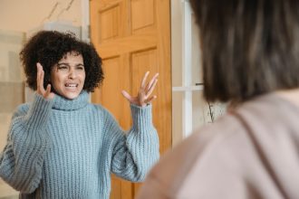 Duas mulheres discutem em um ambiente interno, olhando uma para a outra com expressão de desentendimento.