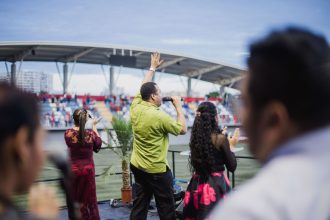 Grupo de artistas se apresenta em um estádio ao ar livre diante do público.