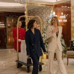 Duas mulheres elegantes caminham pelo saguão decorado de um hotel de luxo.
