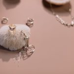 Composição de anéis e um colar prateados dispostos sobre um fundo rosa.