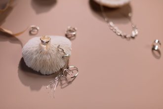Composição de anéis e um colar prateados dispostos sobre um fundo rosa.