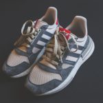 Close de um par de tênis Adidas em tom cinza, com cadarços visíveis.