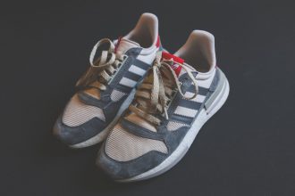 Close de um par de tênis Adidas em tom cinza, com cadarços visíveis.