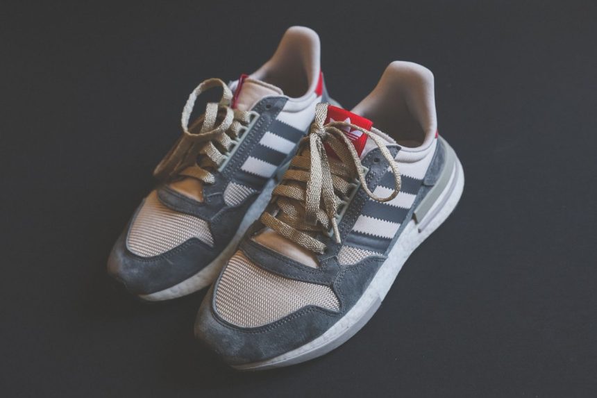Close de um par de tênis Adidas em tom cinza, com cadarços visíveis.